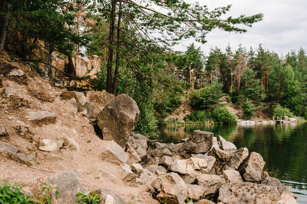 Камни и камни падают в воду. Озеро на фоне скал и елок. Каньон. Место для текста и дизайна. Пейзаж старого затопленного промышленного гранитного карьера, заполненного водой.
