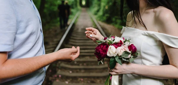Handsome groom makes a proposal to get married the bride. Loving couple on railroad. Tunnel of love with trees and railway.