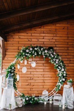 Düğün kemeri, süslenmiş beyaz çiçekler, yeşillikler, yeşillik. Fotoğraf duvarı, yer ya da yer, ahşap duvarın arka planında mumlar. Boho stilinde düğün süsü: Rüya Avcıları.