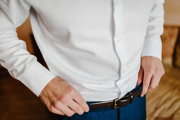 A man in pants and shirt buttoned a leather trouser belt. Groom Dress up a belt with buckle. Businessman wear leather stylish belt. New classic belt.
