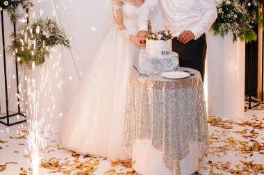 Gelin ve damat düğün ziyafetinde köy pastalarını kesiyorlar. Eller zarif pembe çiçeklerle pastayı keser..