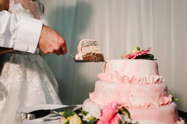 Gelin ve damat düğün ziyafetinde köy pastalarını kesiyorlar. Eller zarif pembe çiçeklerle pastayı keser..