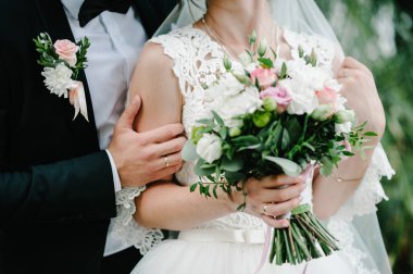 Gelin ve damat, ellerinde bir buketle, doğa bahçesindeki düğün töreninde ayakta duruyorlar..
