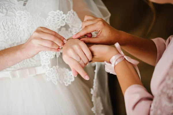 新婦付添人は花嫁のための彼の腕にブレスレットを置くのを助ける 花嫁はジュエリーを身に着けブレスレットに集中する 結婚式のためのブライダル準備 — ストック写真