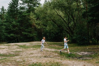 Genç bir çift kaçıyor ve arka planda eğleniyor. Bir kadın kocasını ağaçların ve köknar ağaçlarının arkasında yakalar..
