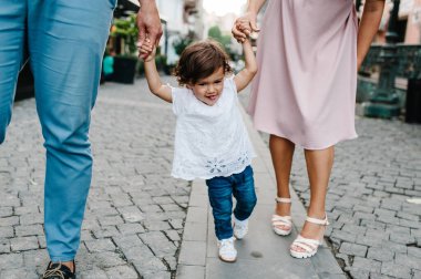 Anne, baba küçük kızı tutuyor. Genç mutlu aile: baba, kız, anne eski şehrin, kasabanın, açık havanın antik mimarisinin yakınında sokaklarda yürüyor. Aile tatili ve seyahat kavramı.