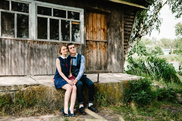 若い夫婦が座って抱き合っていると 木々の間の森の中に窓のある古い木造の家の近くに彼の手の中に閉じられた本を保持します 背景や風景についてです 閉じろ — ストック写真