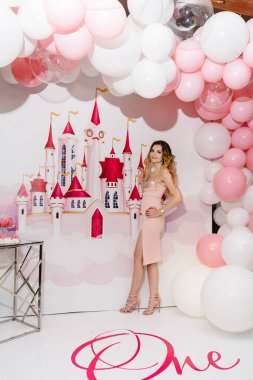 Pembe elbiseli, lüks prensesi olan güzel bir kadın. Fon balonlarında ve şatoda yalnız poz veren muhteşem elbiseli moda kadını. Doğum günü kutlaması kavramı 1 yıldır..