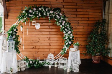 Düğün kemeri, süslenmiş beyaz çiçekler, yeşillikler, yeşillik. Fotoğraf duvarı, yer ya da yer, ahşap duvarın arka planında mumlar. Boho stilinde düğün süsü: Rüya Avcıları.