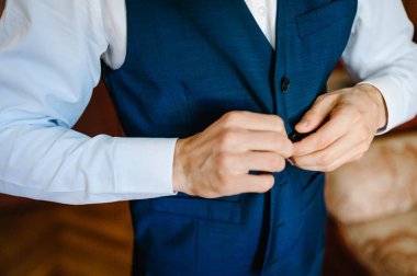 Adam yeleğinin düğmelerini ilikliyor. Yakın plan. En ince ayrıntısına kadar mükemmel. Modern iş adamı. Zarif klasik takım elbiseli yakışıklı bir gencin moda fotoğrafı. Erkek güzelliği, moda.