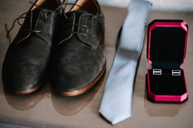 Damat kol düğmeleri bir kutuda, kahverengi erkek ayakkabıları, kravat, masada. Aksesuarcı adamlar. Damadın düğün hazırlığı sabahı..