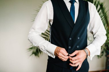 Adam yeleğinin düğmelerini ilikliyor. Yakın plan. En ince ayrıntısına kadar mükemmel. Modern iş adamı. Zarif klasik takım elbiseli yakışıklı bir gencin moda fotoğrafı. Erkek güzelliği, moda.