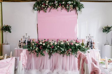 Şölen masası, kemer, pembe çiçekler ve yeşillik kompozisyonu ile süslenmiş, ziyafet salonunda mumlar. Yeni evliler düğün ziyafeti alanında toplandı..