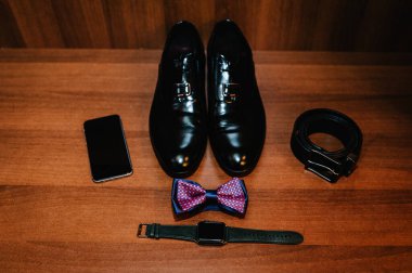 Şık erkek ayakkabıları, saat, damat için papyon. Düğün aksesuarları ve ahşap arka planda telefon. Üst görünüm.