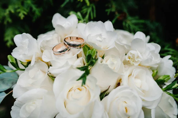 Wedding rings bride and groom on the background bridal bouquet with flowers and white roses and greenery lying on the grass.