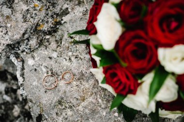 Nişan. Düğün yüzükleri gelin ve damat arka plandaki gelin buketinde. Çiçeklerden yapılmış renkli bir buket gri bir arka planda yatıyor. Taş üstünde gelin buketi. Üst görünüm.
