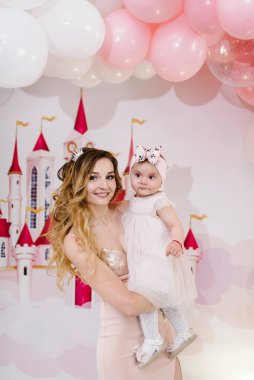 Mutlu aile fotoğrafı: balonların arka planında anne ve kızı. Kadın ve küçük kız prenses. Doğum günü kutlaması kavramı 1 yıldır..