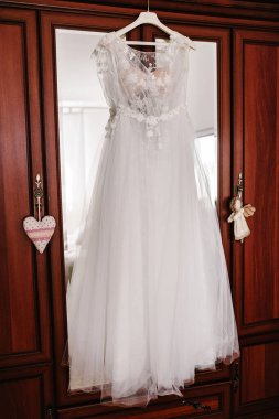 Otel odasındaki ahşap dolapta asılı duran şık dantelli gelinlik. Sabah hazırlığı düğün konsepti.