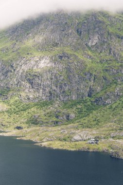 Lofoten, Norveç'te büyük dağlar arasında göl yanındaki küçük ev.