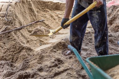 Bir işçi kürek kum içine yeni ev inşaatı için wheelborrow doldurmak için kullanın. İnşaat araçları.
