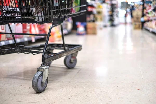 Shopping cart focusing on its wheel in department store, supermarket interior.