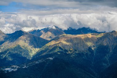 Dağ manzarası. Sıcak sonbahar güneşli bir gün. Dağlarındaki sonbahar ormanları ile kaplı. Bulutlar dağ zirveleri yukarıda. Üstleri karda