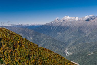 Dağ manzarası. Sıcak sonbahar güneşli bir gün. Dağlarındaki sonbahar ormanları ile kaplı. Bulutlar dağ zirveleri yukarıda. Üstleri karda