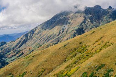 Dağlarındaki sonbahar orman çalılar ve otlar ile kaplıdır. Renkli sonbahar manzara. Sıcak sonbahar güneşli bir gün. Bulutlar dağların üzerinden