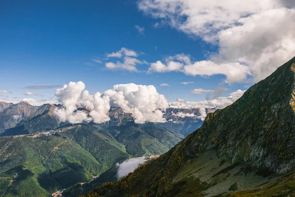 Dağ manzarası. Sıcak sonbahar güneşli bir gün. Dağlarındaki sonbahar ormanları ile kaplı. Bulutlar dağ zirveleri yukarıda. Üstleri karda