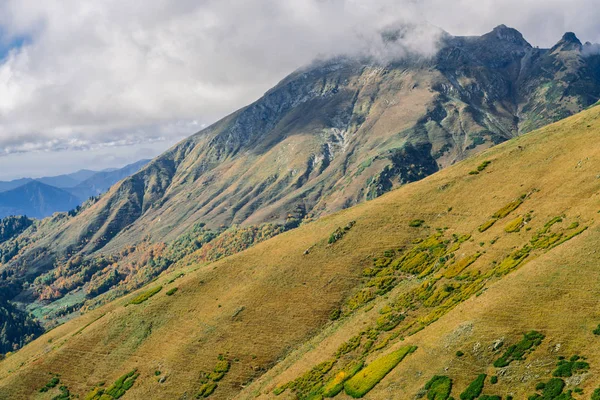Dağlarındaki sonbahar orman çalılar ve otlar ile kaplıdır. Renkli sonbahar manzara. Sıcak sonbahar güneşli bir gün. Bulutlar dağların üzerinden