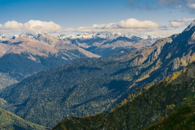 Dağ manzarası. Sıcak sonbahar güneşli bir gün. Dağlarındaki sonbahar ormanları ile kaplı. Bulutlar dağ zirveleri yukarıda. Üstleri karda