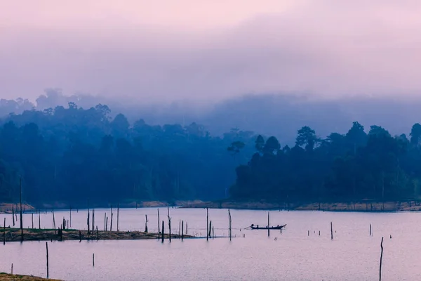 The boat sails on the lake at dawn. Lake Cheo LAN in the national Park Khao SOK in Thailand. On the background of mountains and clouds. The pre-dawn sky. The fog over the mountains