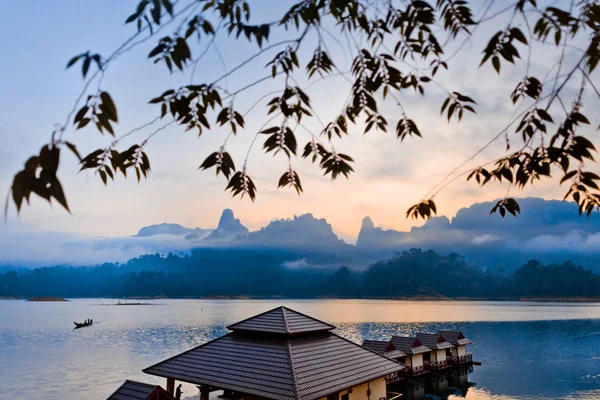 Bungalow on the lake at dawn. Tree branches in the foreground. On a background of dawn over the mountains, the lake and the fog. Lake Cheo LAN in the national Park Khao SOK in Thailand