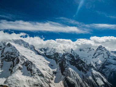 Dağ zirveleri karla kaplı. Güneşli bir günde karlı dağlar. Bulutların üzerinde dağ başında. Güzel dağ arka plan