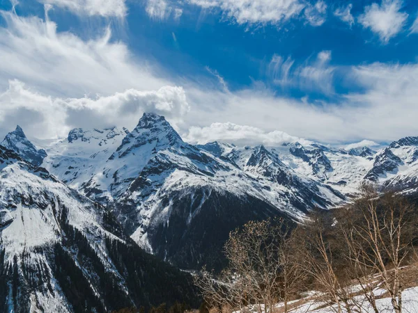 Mountain peaks covered with snow. Sunny day in the snowy mountains. Clouds above the mountain tops. Beautiful mountain background