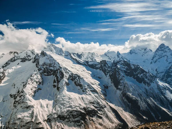 Mountain peaks covered with snow. Sunny day in the snowy mountains. Clouds above the mountain tops. Beautiful mountain background