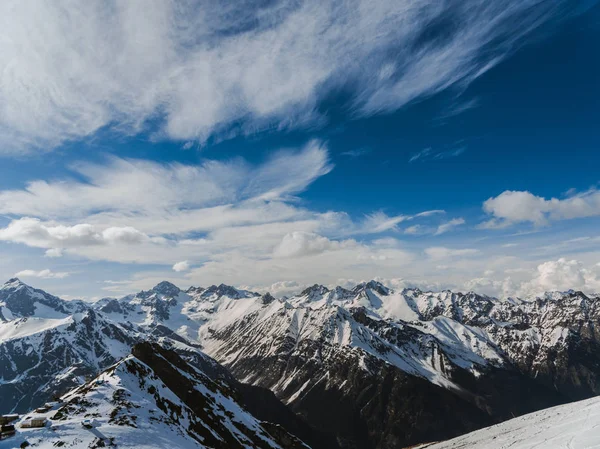 Mountain peaks covered with snow. Sunny day in the snowy mountains. Clouds above the mountain tops. Beautiful mountain background