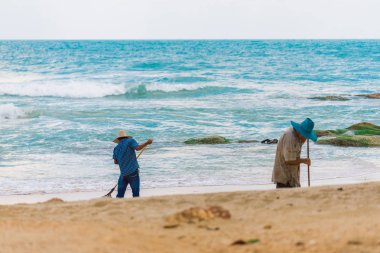Erkekler beach Koh Samui çöpleri. İki erkek yaprakları okyanus arka plan üzerinde bir komisyon ile toplamak. Thais temiz plaj