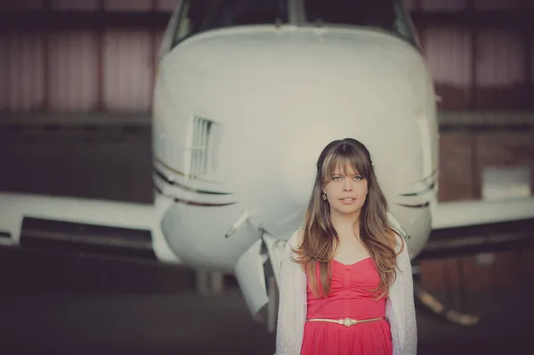 Alone woman with red dress in the background a plane in a hangar.