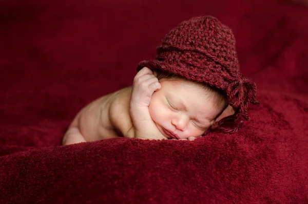 Newborn girl wears a red crochet hat while sleeping in the bed with a red background. Selective Focus