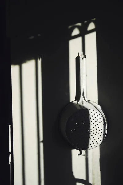 White metallic strainer illuminated with natural light and shadows