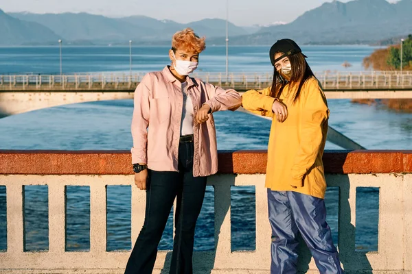 Teenage friends wearing face masks showing a new way of welcoming during the Covid virus. Concept of new normal and social distancing