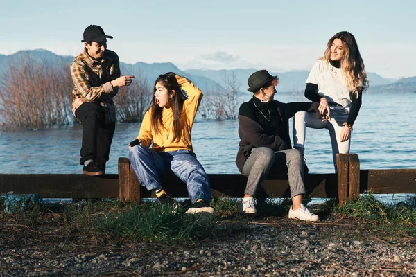 Four millennials friends near to a lake have fun posing for photos. Modern youth fashion and lifestyle.