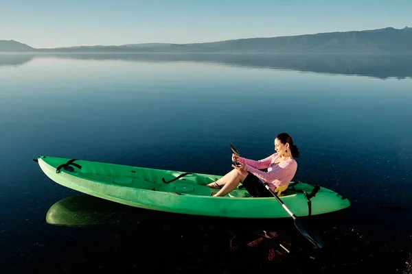 Caucasian woman floating in a kayak and using her phone to take pictures and videos of the landscape. Enjoying her freedom. Copy space