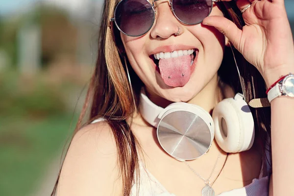 Beautiful woman with sunglasses and headphones sticking out her tongue and showing a piercing on a summer day. Concept of enjoyment and lifestyle