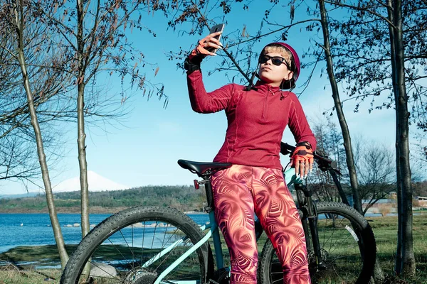 Woman cyclist with helmet resting and taking a selfie in a natural park during the summer