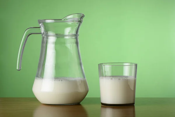 Glass of milk and jar on green background