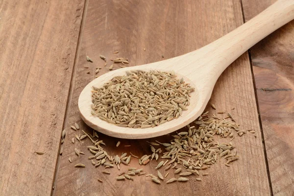 Cumin beans in a wooden spoon on wooden background, seeds