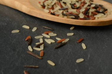 Üç renkli pirinç (buğulanmış, kırmızı ve siyah) siyah bir arka planda tahta bir kaşıkta, üst görünümde.