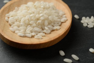 Siyah taş zemin üzerinde tahta bir kaşıkta yuvarlak beyaz pirinç, detay veya makro